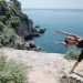 A woman in activewear stretches on a cliff by the ocean, embracing coastal fitness.