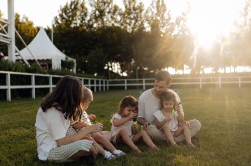 Family sitting on grass enjoying leisure time outdoors, with sun setting in the background.