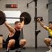 Athlete performing weightlifting exercise under trainer's guidance in a gym setting.